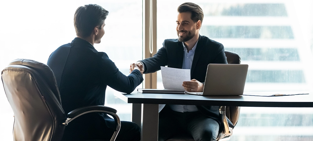 smiling businessmen shake hands with insurance agent in office