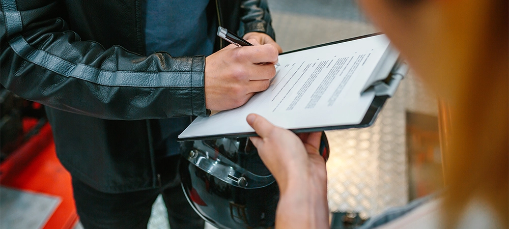 Unrecognizable biker man wearing leather jacket and holding helmet signing insurance policy to receipt his repaired motorcycle on workshop
