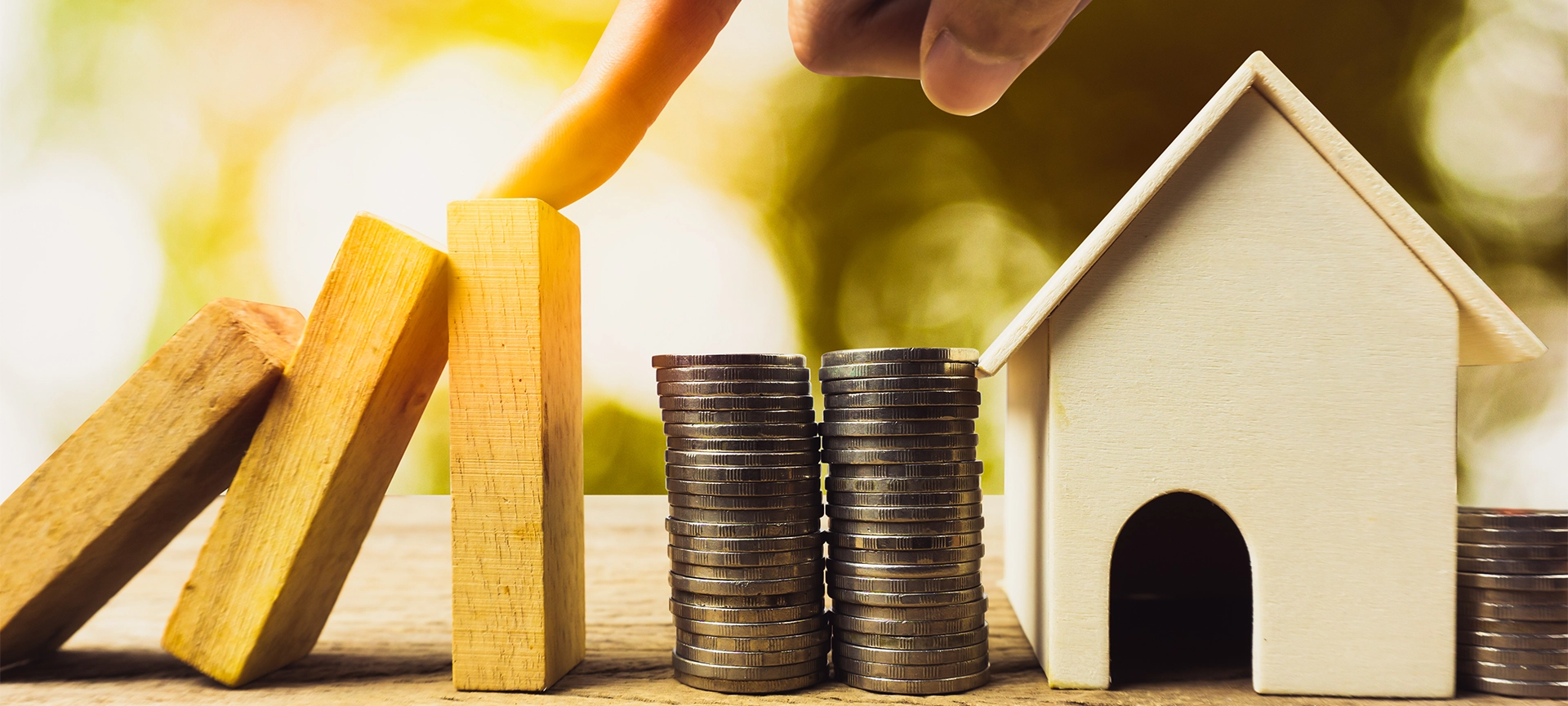 Home or real estate insurance protection concept. A man hand stop a wooden dominoes continuous toppled before reaching the house and money. Depicts preventing losses that will occur to the property.