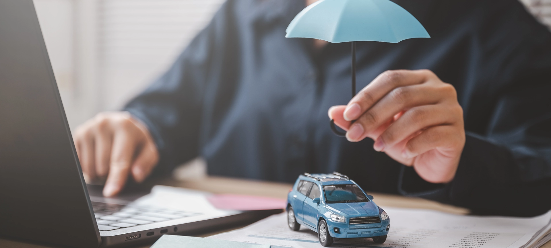 Car insurance protect safe transport. Safety trust. Protection secure assurance. A woman is holding a blue umbrella over a toy car on a desk.
