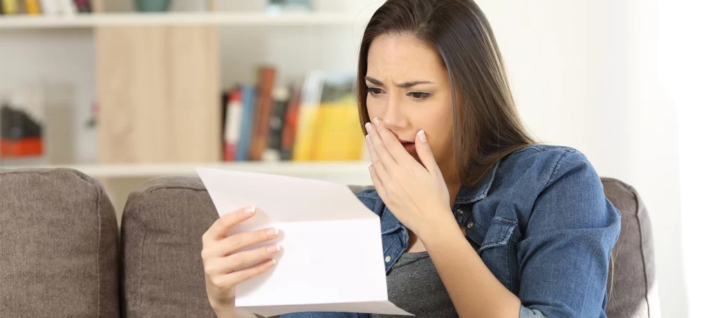 Sad woman reading bad news in a paper letter sitting on a couch in the living room at home